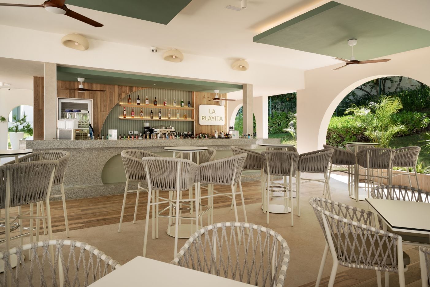 ar abierto al aire libre «La Playita» con barra de servicio de obra, taburetes de cuerda tejida en color beige y arcos que dan hacia los jardines tropicales