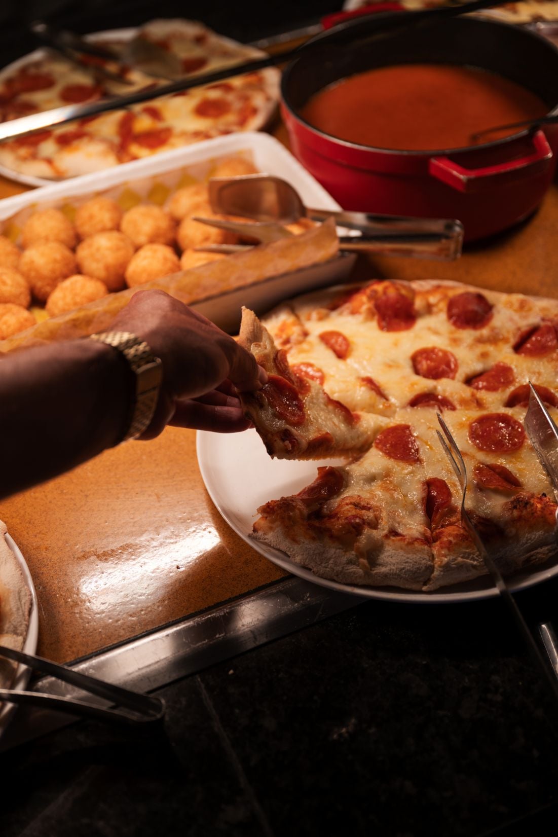 Una mano coge un trozo de pizza con pepperoni del restaurante italiano de RIU