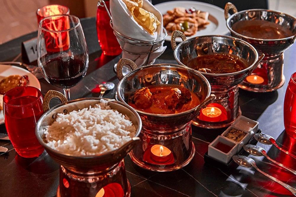 Platos de cocina india en cuencos de cobre con velas, arroz basmati y copas de vino en el hotel Riu Turquoise