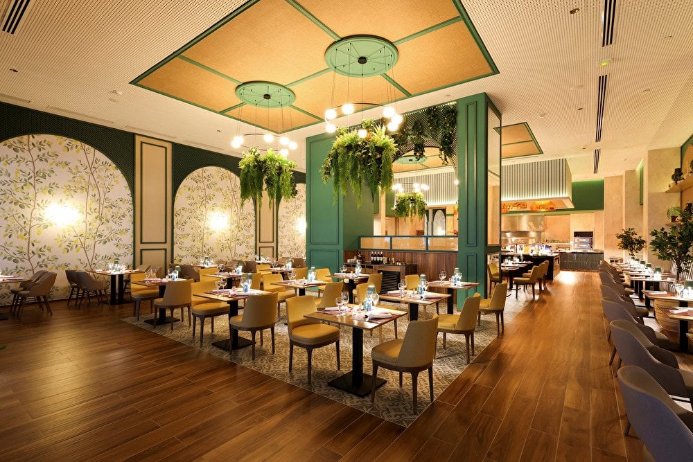 Comedor de restaurante con sillas amarillas, lámparas con plantas colgantes y suelos de madera en el hotel Riu Ventura