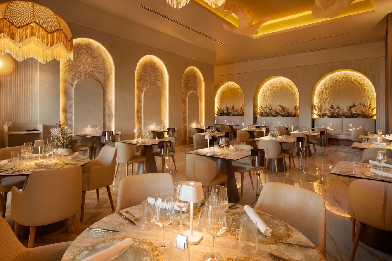 Elegante restaurante «Krystal» de diseño refinado, con iluminación cálida indirecta, paredes con relieve de palmeras iluminadas, vajilla de cristal y lámparas de estilo natural