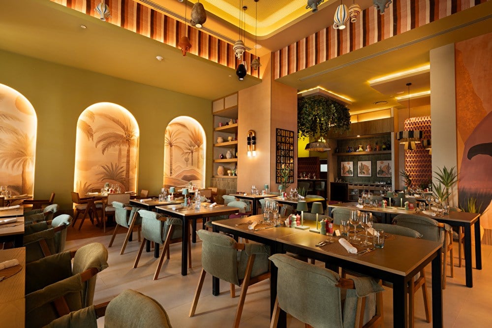 Comedor con murales de palmeras, vajilla montada y vasijas de barro colgantes en el hotel Riu Palace Peninsula