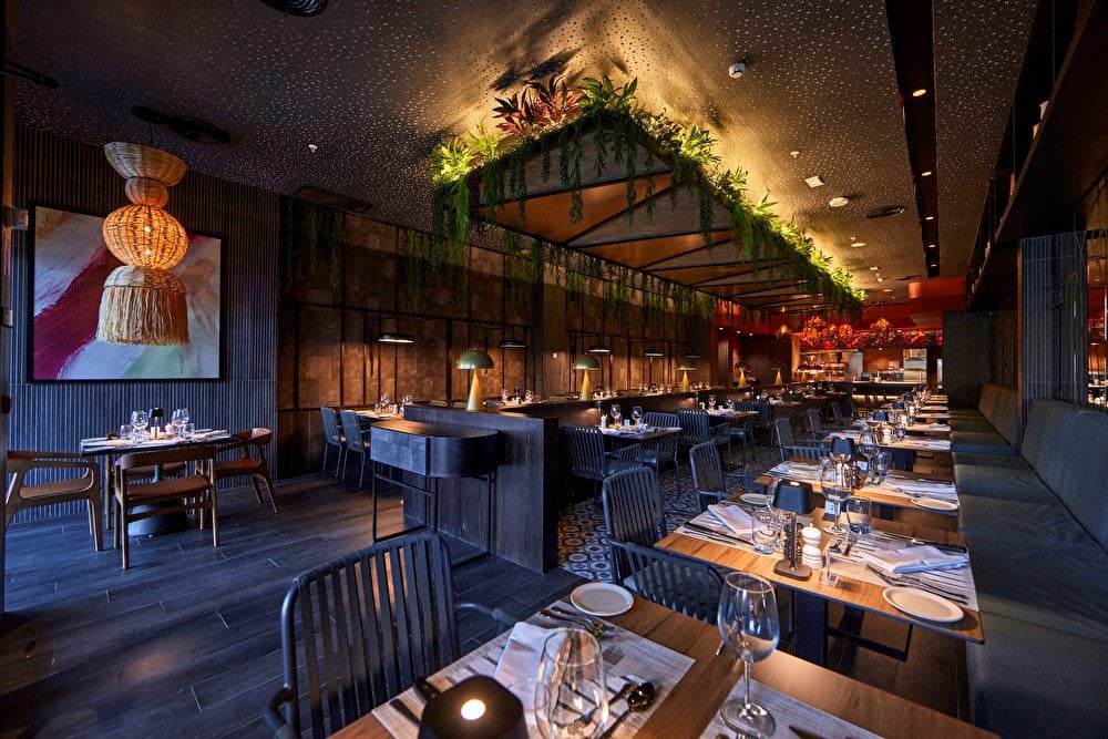 Comedor de estilo oscuro con mesas de madera, lámparas de mesa y plantas en el techo en el Steak House de Riu Turquoise