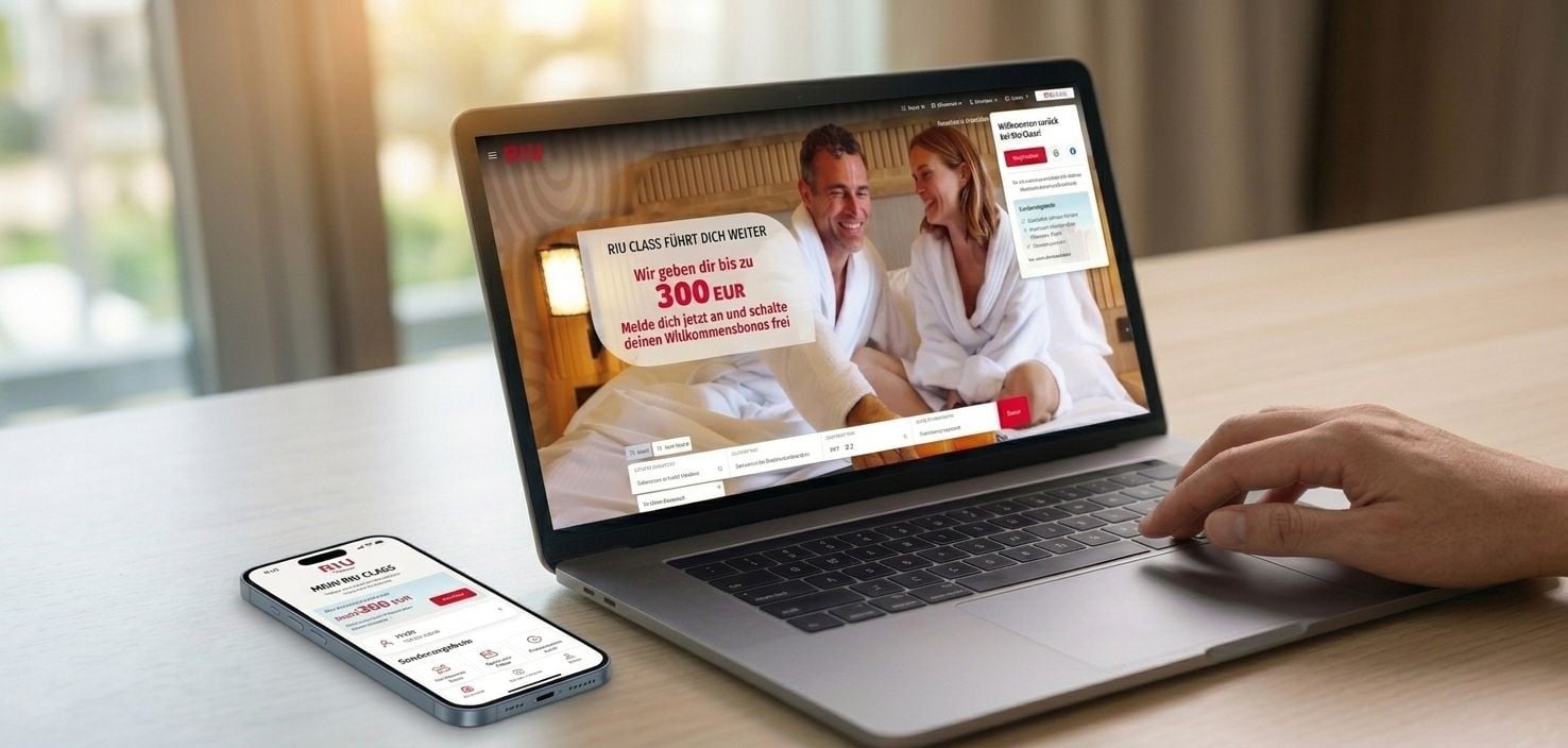 Ein aufgeklappter Laptop und ein Smartphone auf einem Holztisch zeigen die Website und die App von RIU Class mit einem Willkommensangebot von bis zu 300 EUR. Eine Hand ruht auf der Tastatur des Laptops.