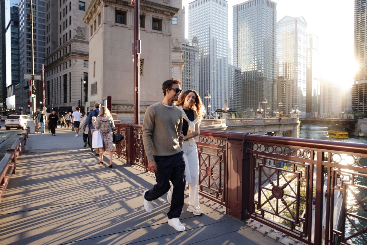 Pareja paseando por un puente con el skyline urbano de fondo cerca de un hotel RIU Plaza.