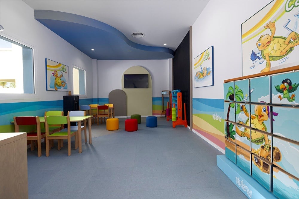 Interior del club infantil RIU Land, en el Riu Palace Aruba en elq ue se ve mesas para niños, un mini teatro, cojines de colores e imágenes de la mascota Calú en la pared