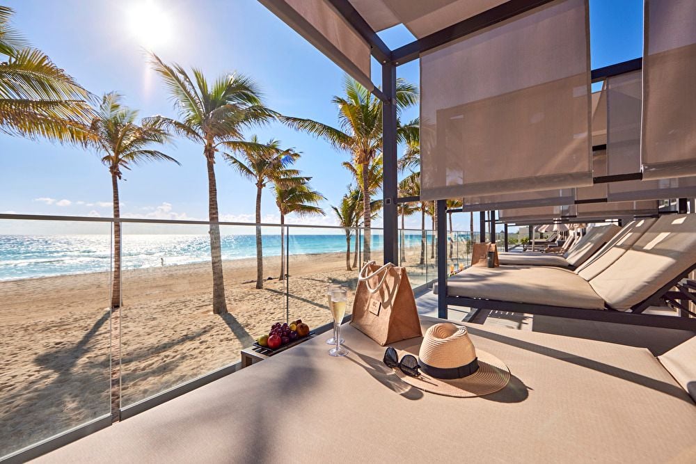 amas balinesas en una terraza privada con vista panorámica a la playa de arena blanca, palmeras y el mar.