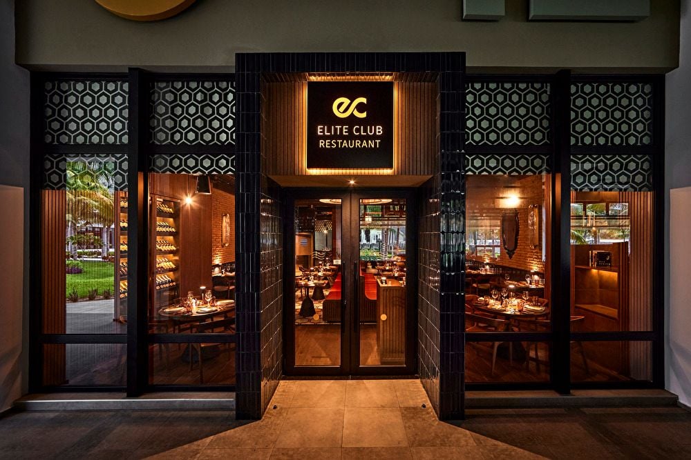 Fachada exterior del restaurante Elite Club con ventanales iluminados y diseño moderno.