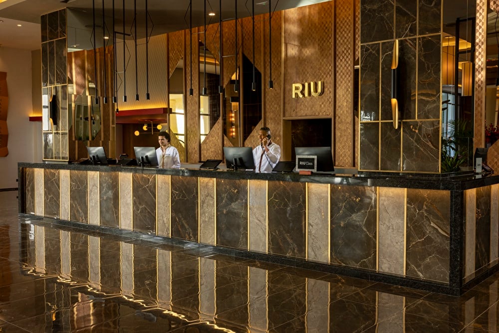 Plano general de la recepción del hotel que muestra la decoración elegante y de lujo. También hay dos recepcionistas posando sonrientes