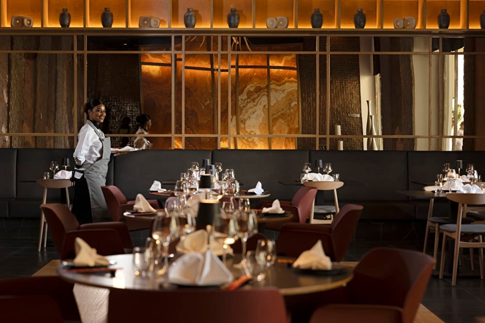 An image featuring a close-up of a table at the Sayuri Asian restaurant, with a waitress setting another table in the background.