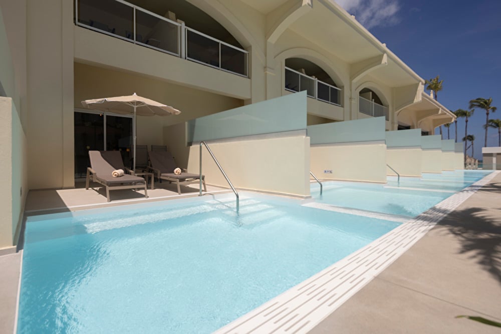 Private pool of a suite at Riu Palace Aruba, featuring two lounge chairs with an umbrella.