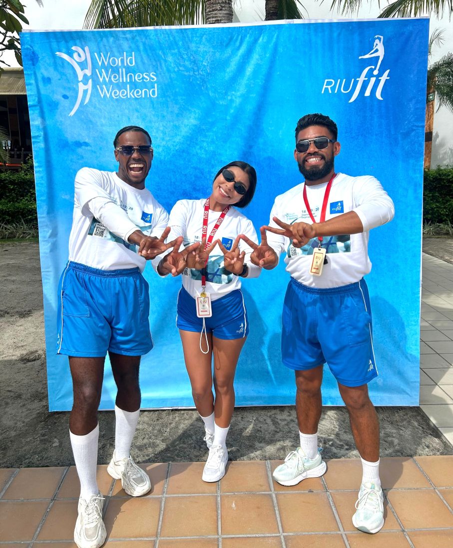 Equipo de monitores RIUfit celebrando el World Wellness Weekend en un resort de playa, vistiendo uniformes deportivos y medallas