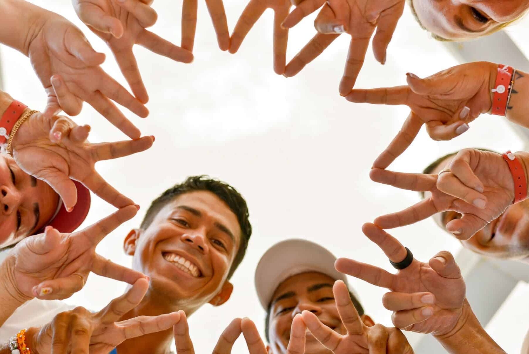 Plano contrapicado de huéspedes y animadores uniendo sus manos en círculo formando la figura de una estrella frente a la cámara en el Hotel Riu Guanacaste