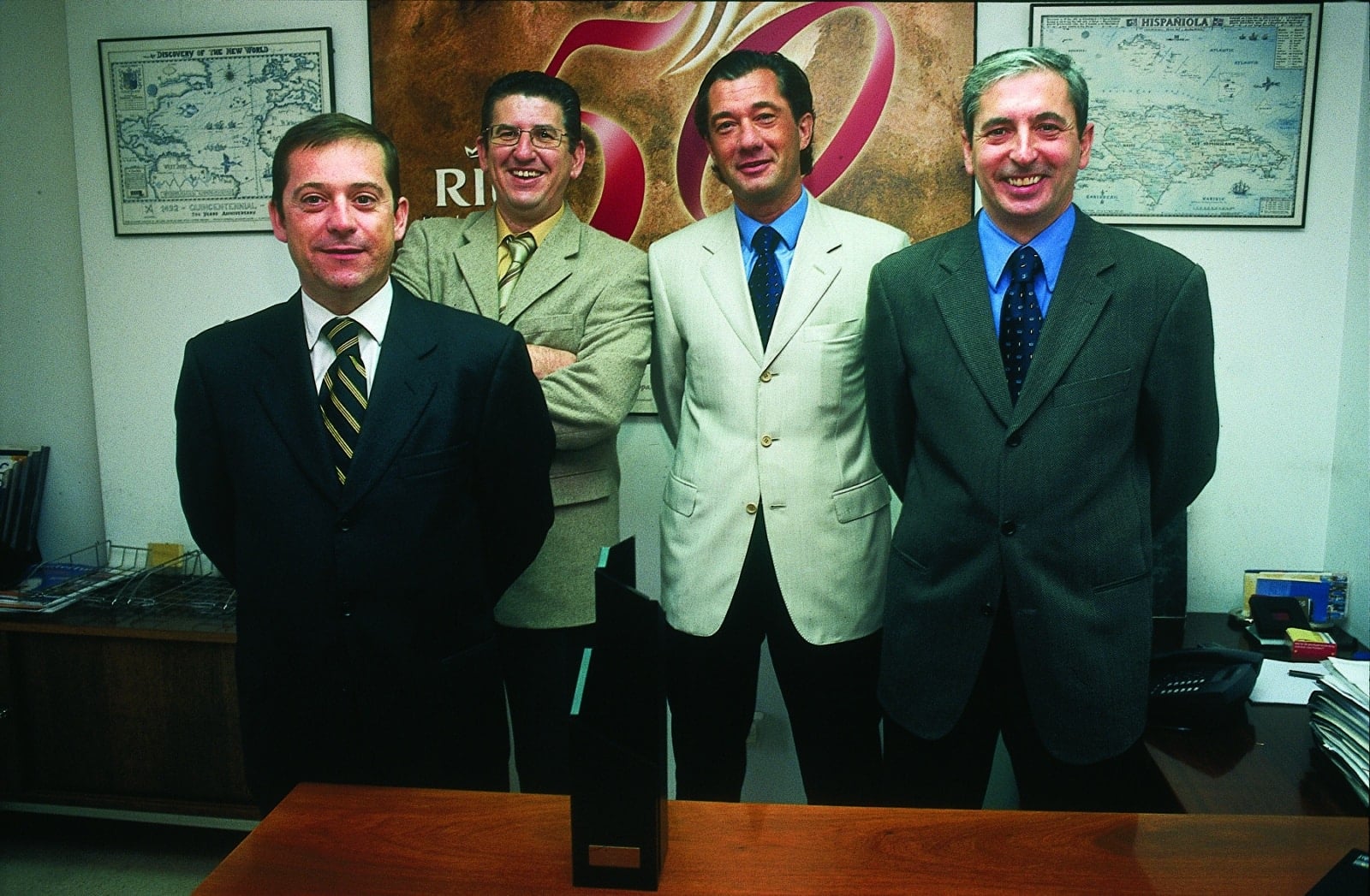 Cuatro directivos de RIU Hotels & Resorts en un despacho ante el cartel del 50 aniversario de la compañía, en 2003