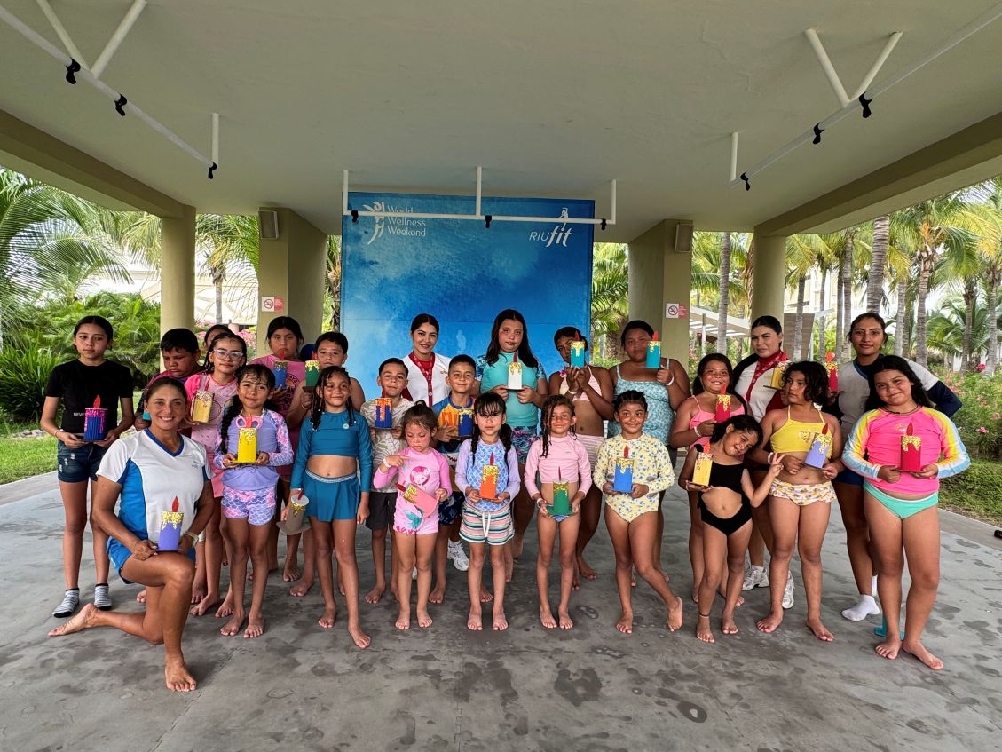 Grupo de niños y monitores posando sonrientes con sus manualidades frente a un photocall de World Wellness Weekend y RIUfit en el Hotel Riu Emerald Bay