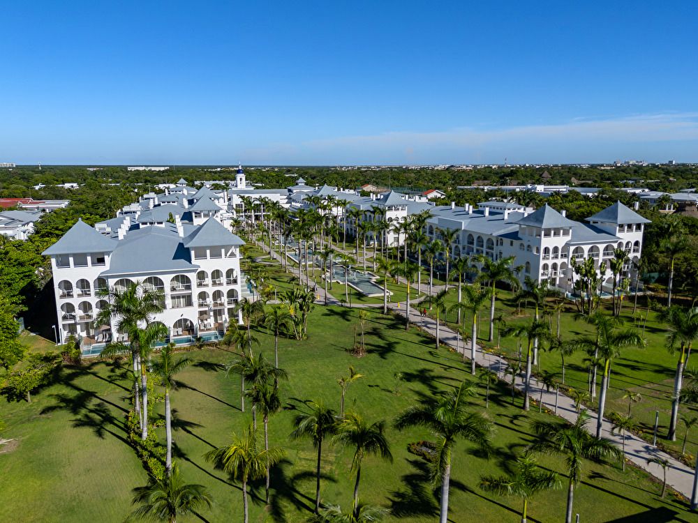 Vista panorámica aérea del complejo Riu Palace Mexico, destacando sus múltiples piscinas, terrazas con tumbonas, palmeras y edificios frente al mar.