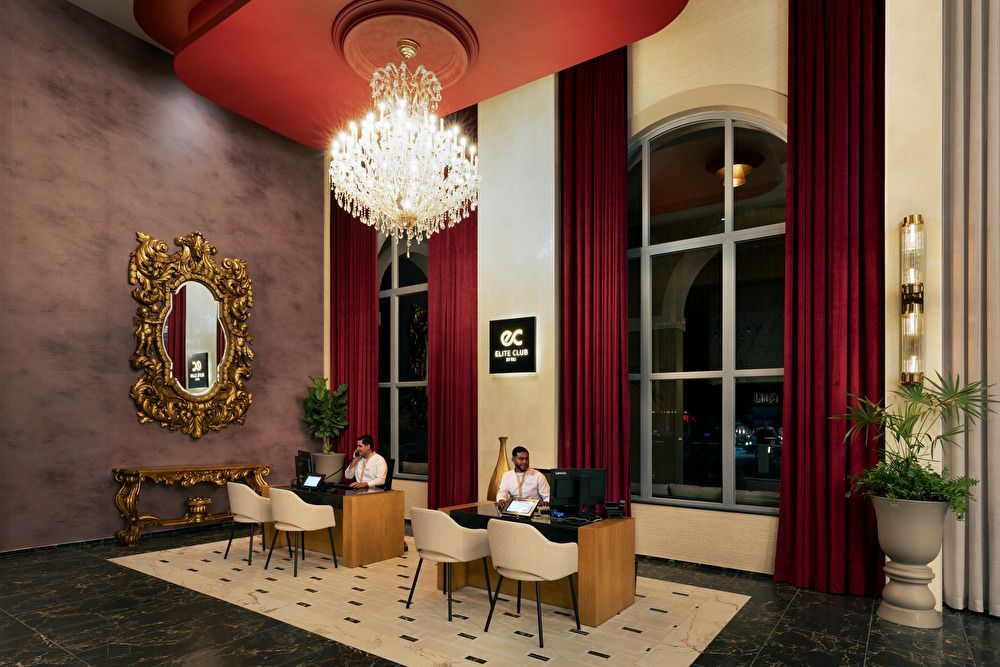 Área de recepción del servicio Elite Club en el Riu Palace Mexico, con cortinas de terciopelo rojo, una araña de cristal, espejo dorado y escritorios de atención personalizada.