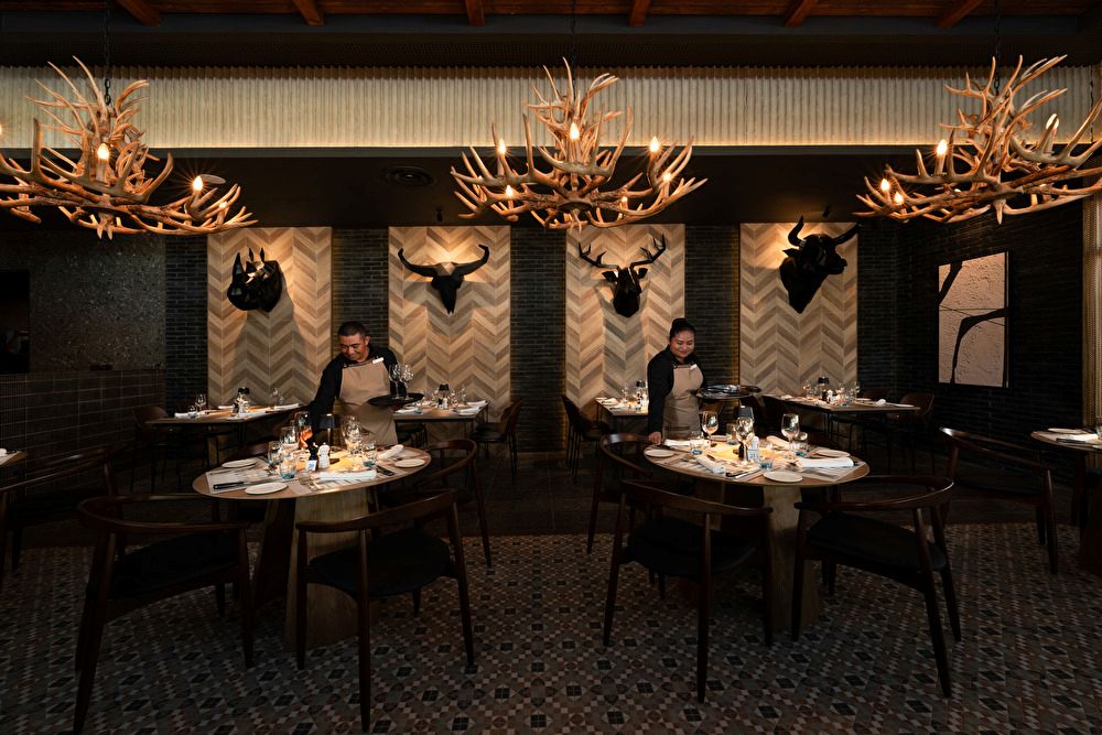 Interior del restaurante Steakhouse en el Riu Palace Mexico, decorado con lámparas de astas de ciervo, cabezas decorativas de animales en las paredes y mesas preparadas para cenar.