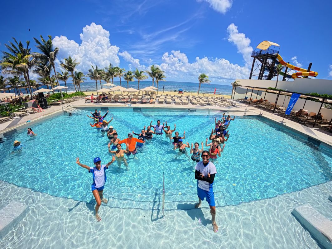 Vista aérea de huéspedes y monitores en la piscina formando la letra W durante una actividad de RIUfit en el Hotel Riu Ventura