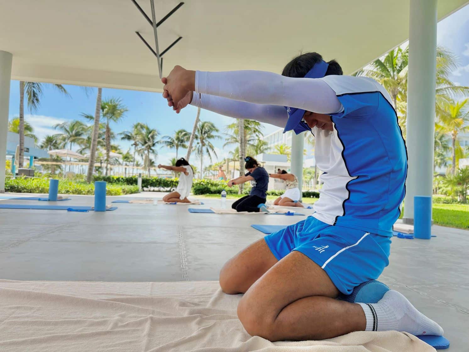 Monitor dirigiendo un estiramiento de brazos y espalda en una sesión de yoga RIUfit en la terraza del Hotel Riu Dunamar