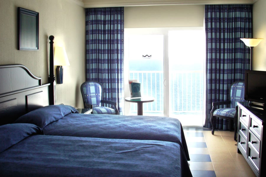 Bedroom with queen bed, blue bedding, balcony doors overlooking ocean, blue curtains.