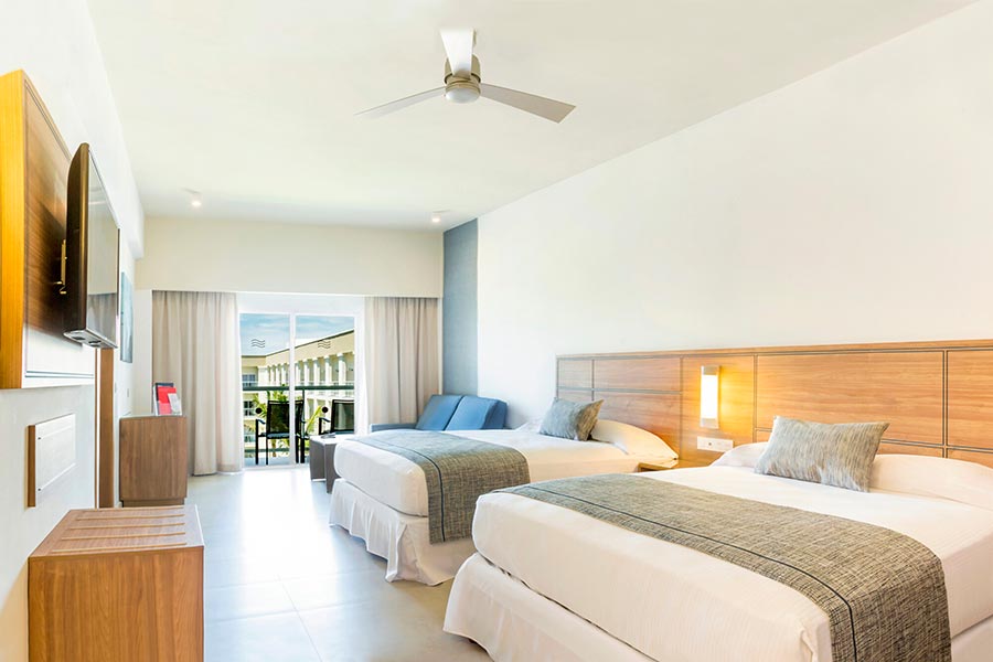 Two double beds with white linens, wood headboards, balcony doors, modern furnishings.