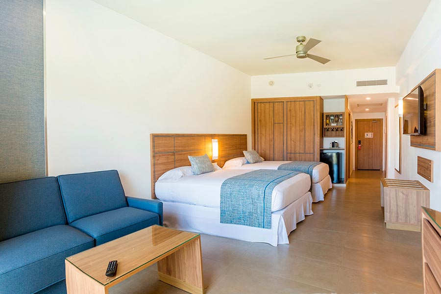 Double beds with blue runners, wood headboard, sofa seating, kitchenette visible.