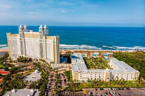 Aerial view of beachfront resort complex with ocean, sandy beach, palm trees.